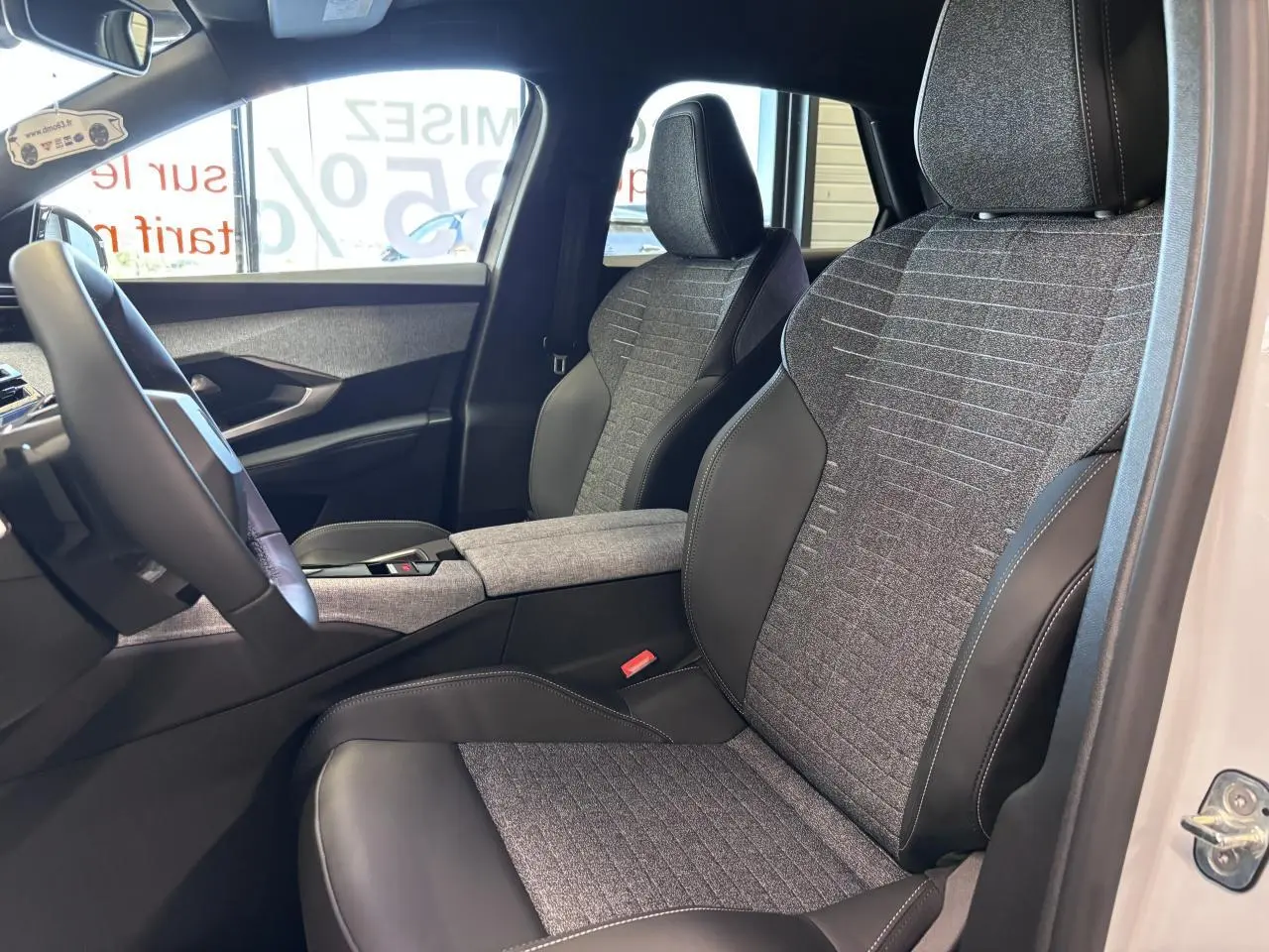 Vue intérieure côté conducteur du Peugeot 3008 blanc 2026, sièges tissu gris et cuir noir avec accoudoir central.