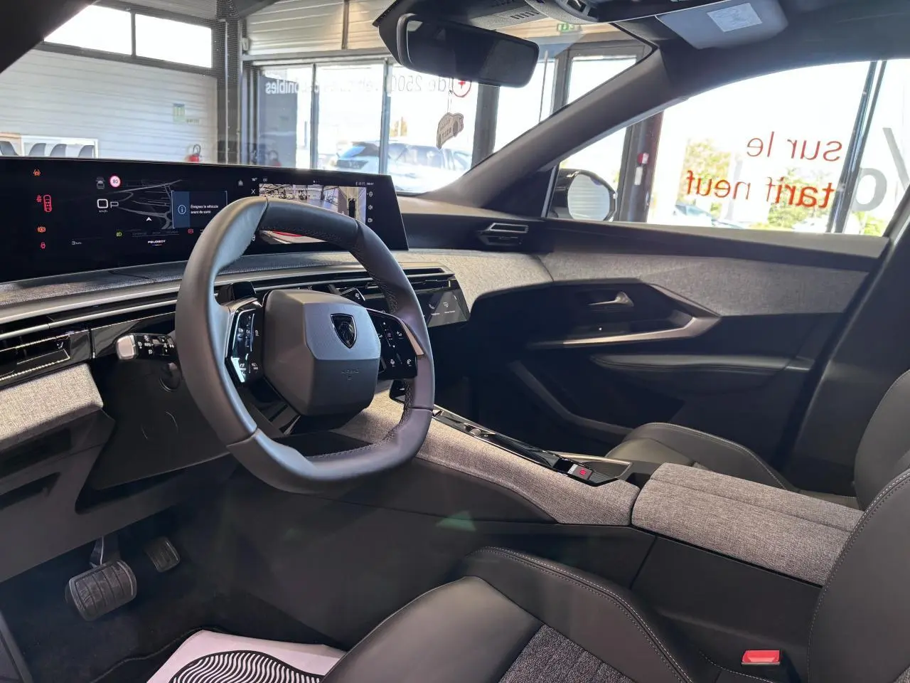 Vue intérieure côté conducteur du Peugeot 3008 Hybrid 2026, avec volant compact, tableau de bord numérique et habillage tissu gris chiné.