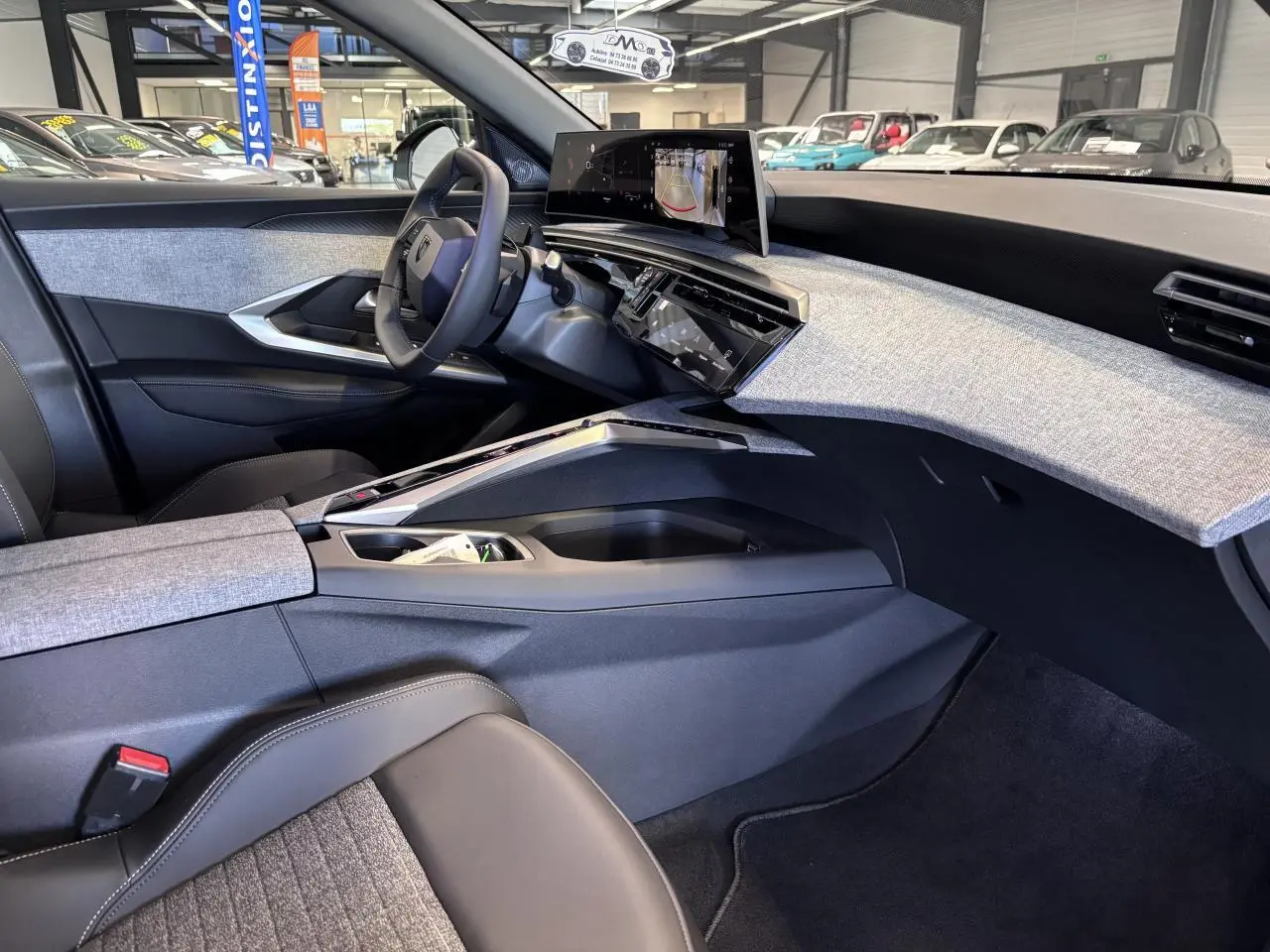 Vue intérieure côté conducteur du Peugeot 3008 Hybrid 2026, tableau de bord avec décor tissu gris et écran incurvé flottant.