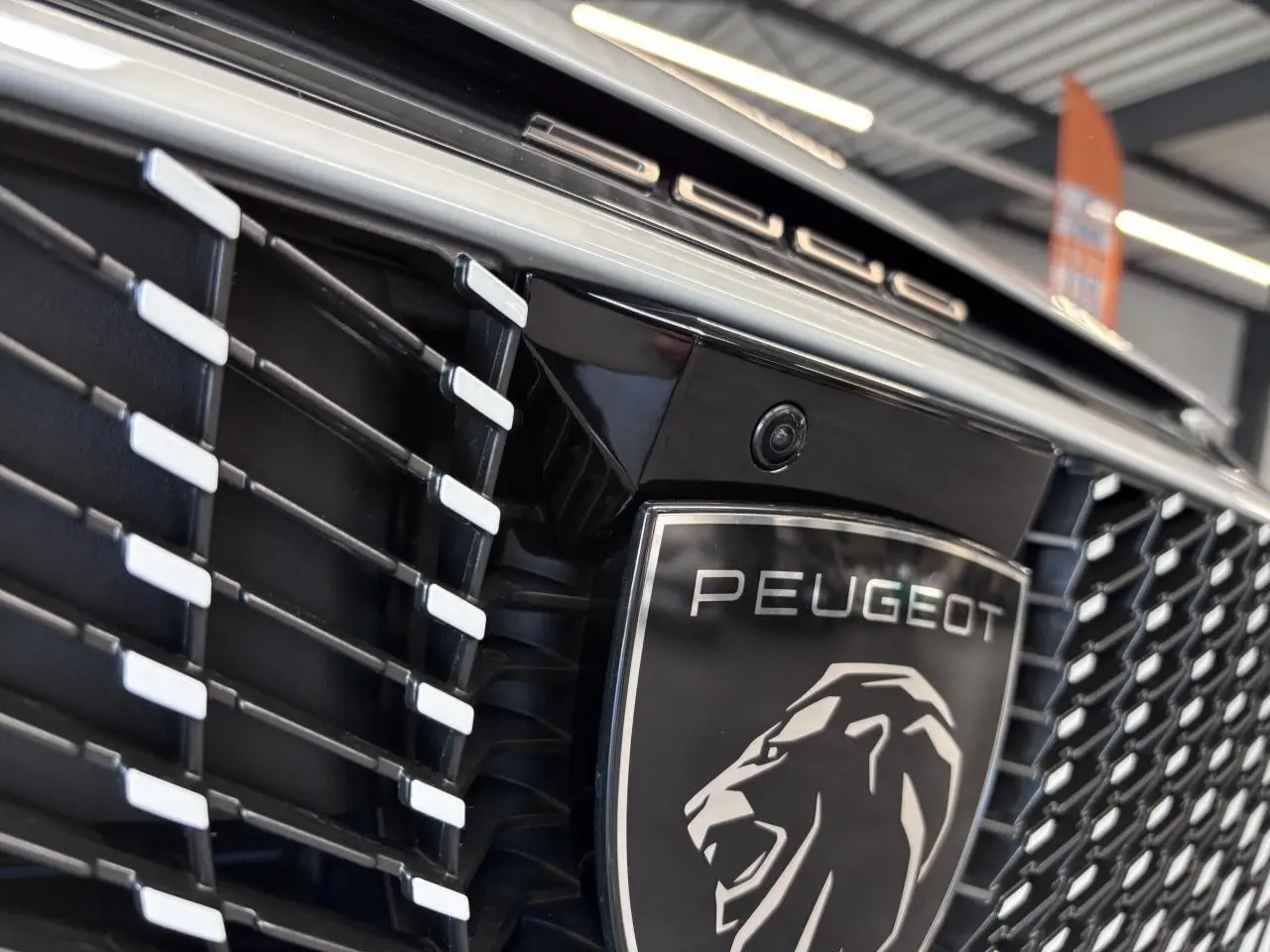 Gros plan sur la calandre noire laquée avec logo Peugeot argenté et caméra frontale du Peugeot 3008 blanc.