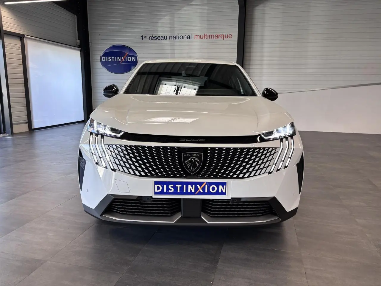 Vue avant d’un Peugeot 3008 blanc avec calandre noire laquée et feux LED à 3 griffes, en intérieur showroom.