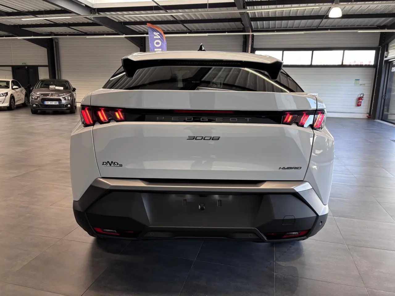 Vue arrière d'un Peugeot 3008 hybride blanc avec feux LED 3 griffes et bandeau noir laqué au showroom.