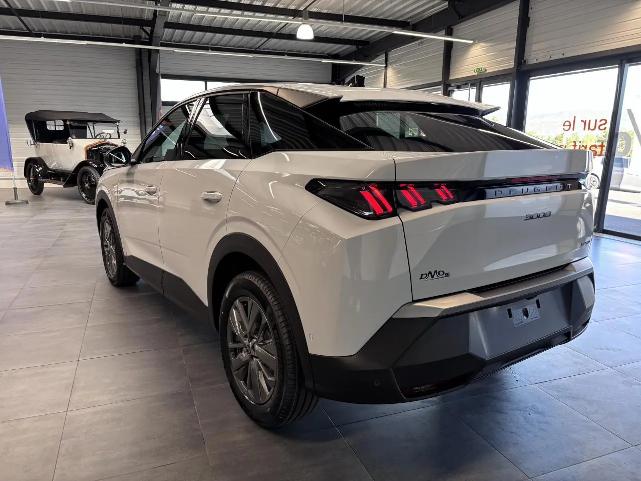 Vue 3/4 arrière droite d'un Peugeot 3008 blanc avec feux arrière LED à 3 griffes et bandeau noir laqué.