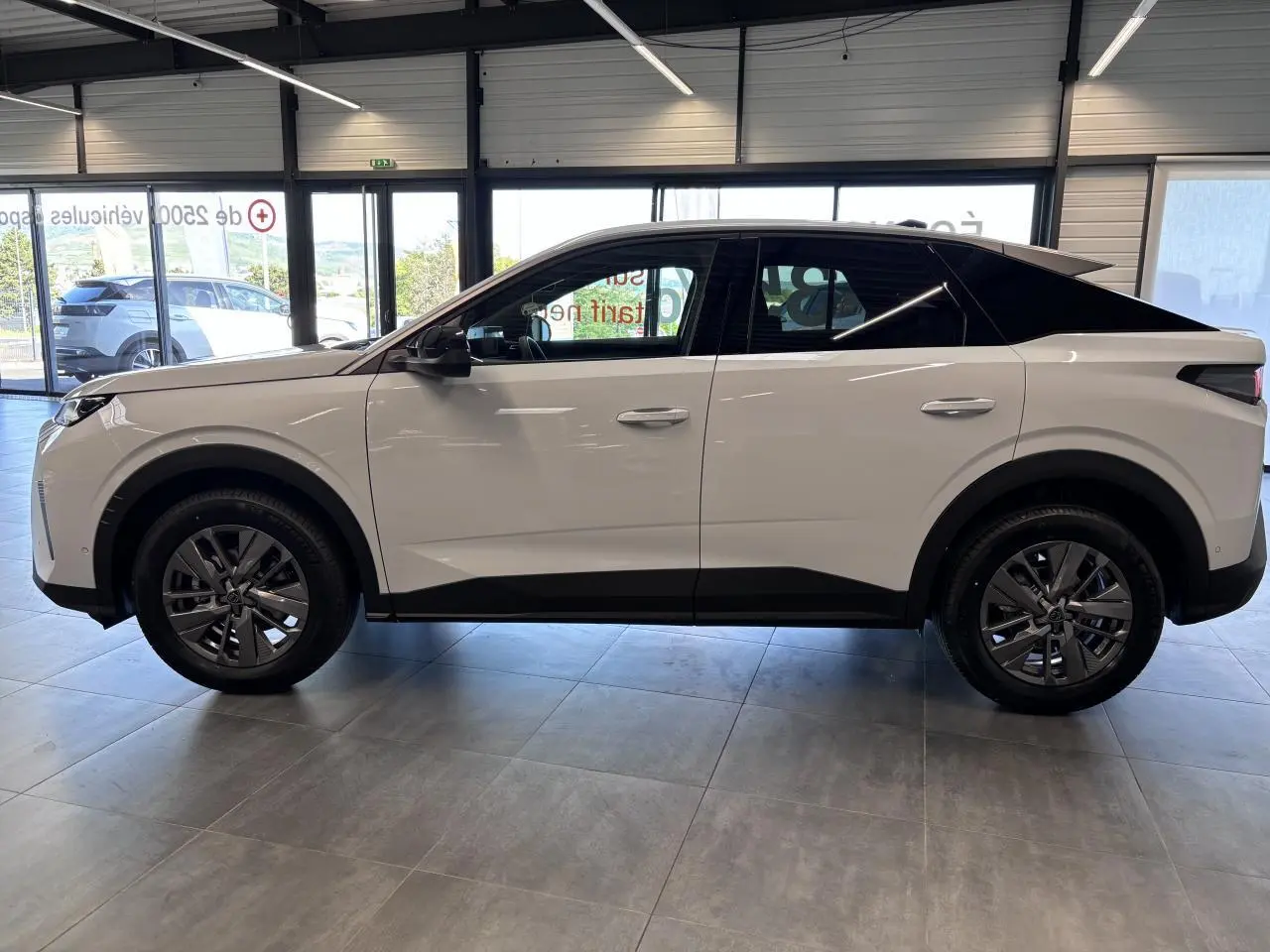 Profil côté gauche d'un Peugeot 3008 blanc avec toit noir et jantes alliage 18 pouces dans un showroom.