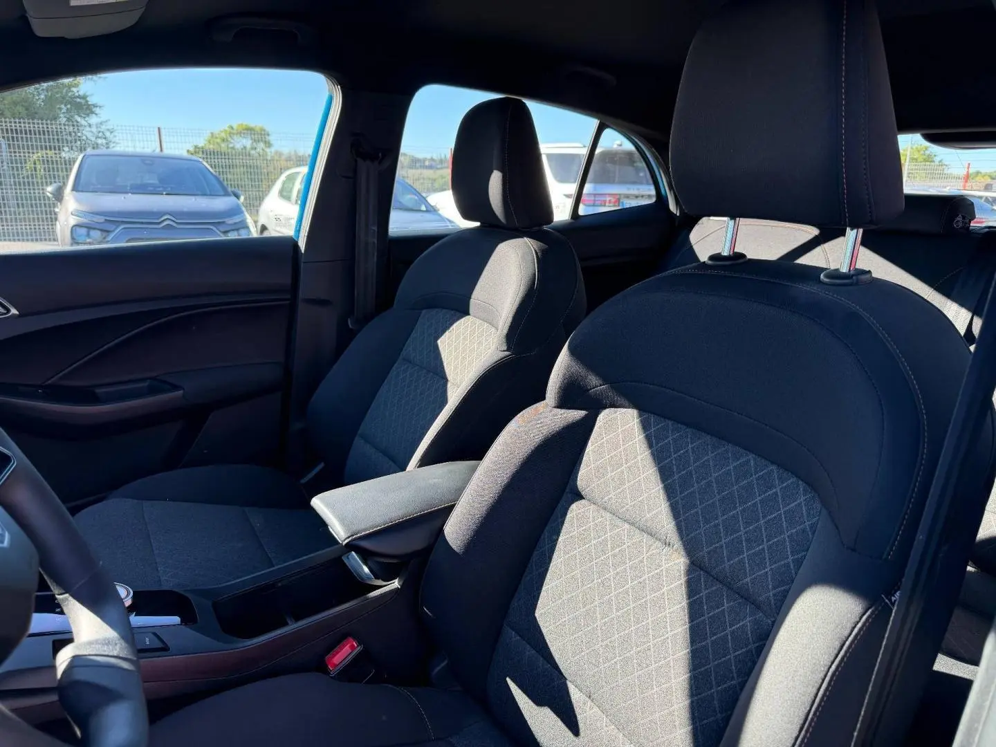 Vue intérieure côté avant droit du MG3 1.5 Hybrid+ 2024 avec sièges tissu noir et accoudoir central.