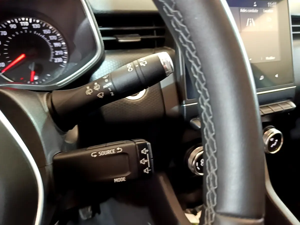 Gros plan sur le volant cuir synthétique et les commandes multifonctions de la Renault Clio Business TCe 100 blanche, tableau de bord visible.