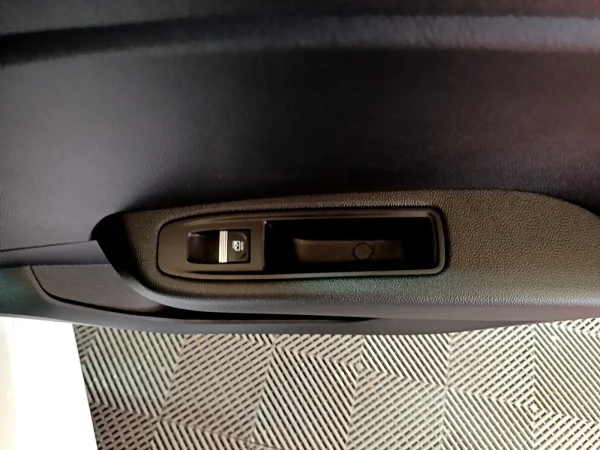 Détail de la commande de lève-vitre électrique sur la porte intérieure noire côté gauche d'une Renault Clio blanche.