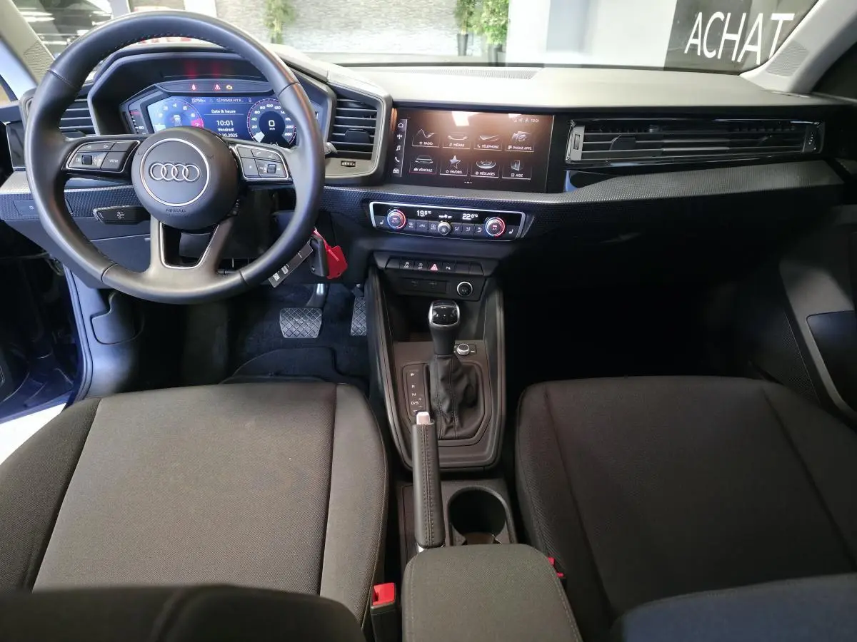Intérieur Audi A1 Sportback 2024 vu de face, tableau de bord noir avec écran digital et volant cuir multifonctions.