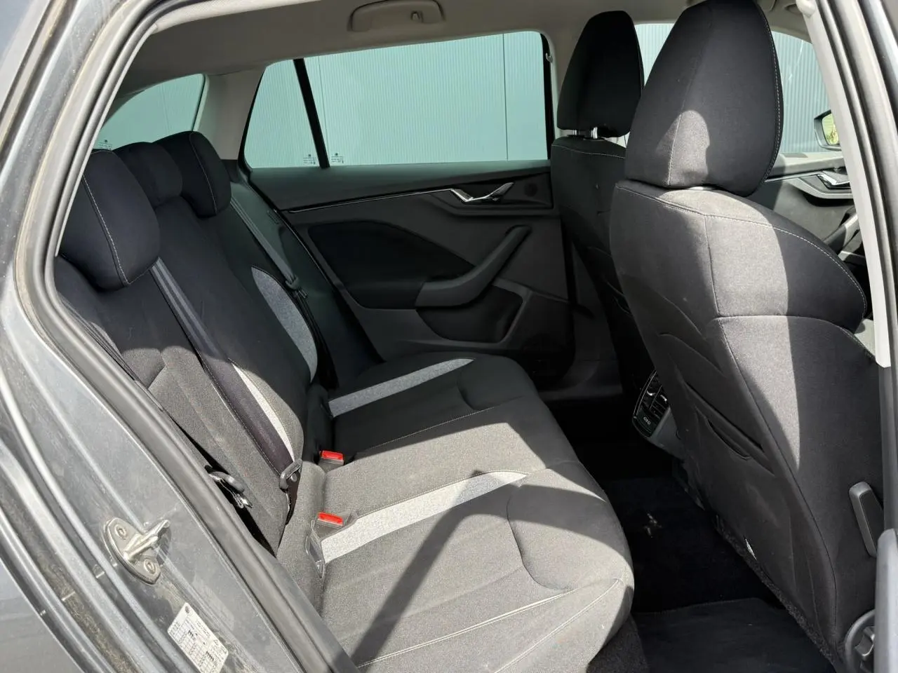 Vue intérieure arrière côté gauche de la Skoda Scala TSI 116 gris graphite, sièges tissu noir avec surpiqûres claires.