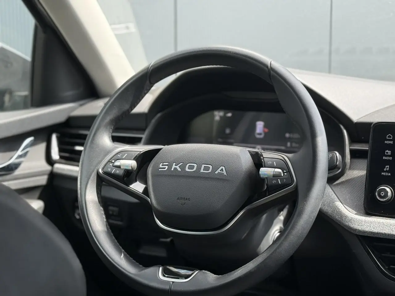 Vue rapprochée du volant cuir noir multifonctions avec logo SKODA, tableau de bord et écran tactile visibles en arrière-plan.