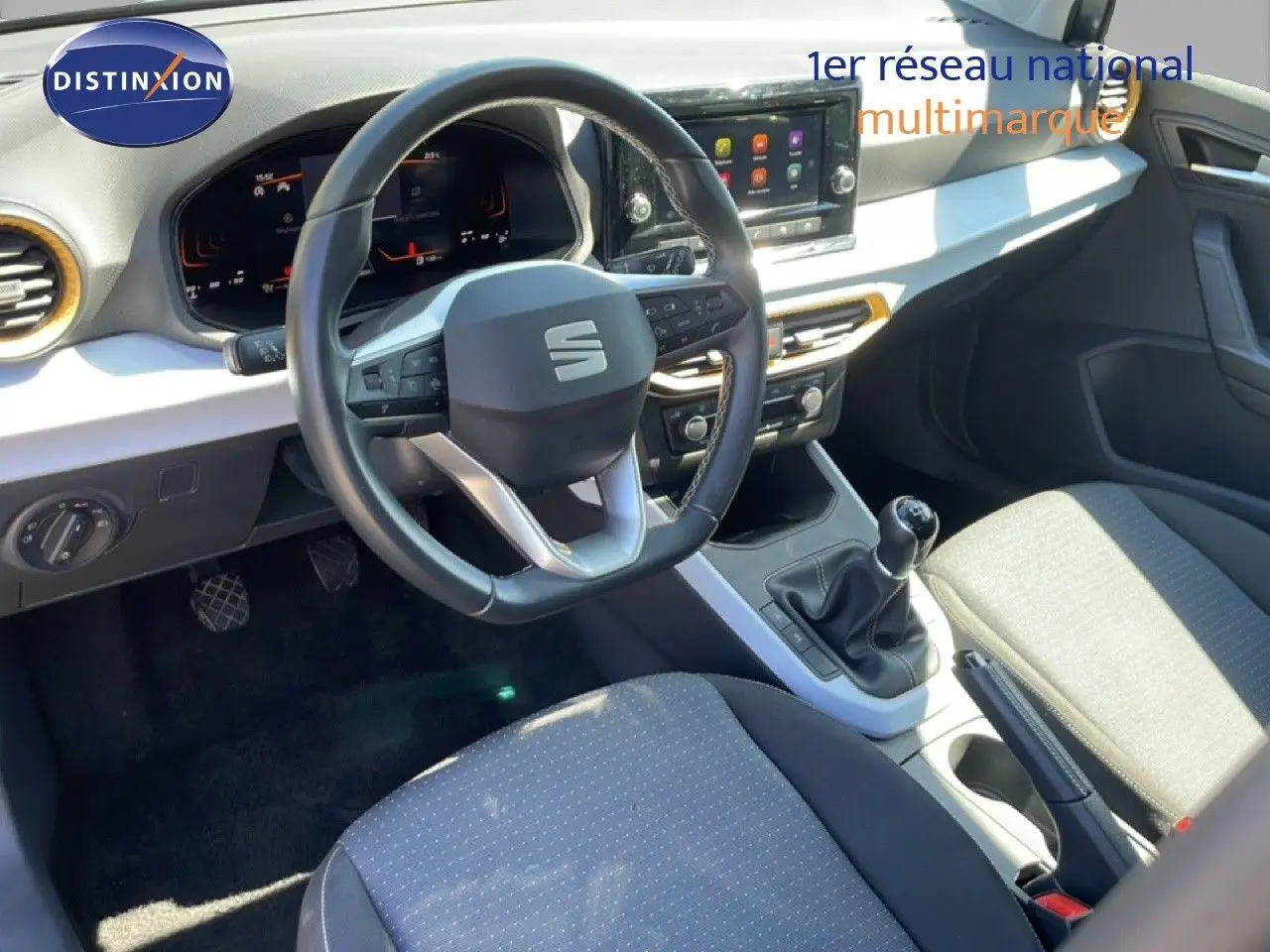 Vue intérieure de face du poste de conduite du SEAT Arona 2025, volant cuir noir, tableau de bord digital et levier de vitesse manuel.
