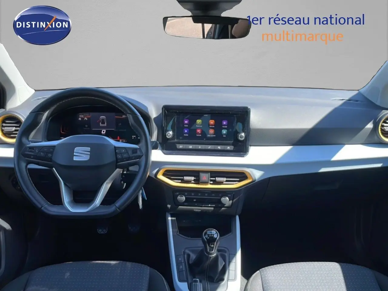 Vue intérieure avant du SEAT Arona 2025, tableau de bord gris clair avec touches dorées et volant multifonction noir.