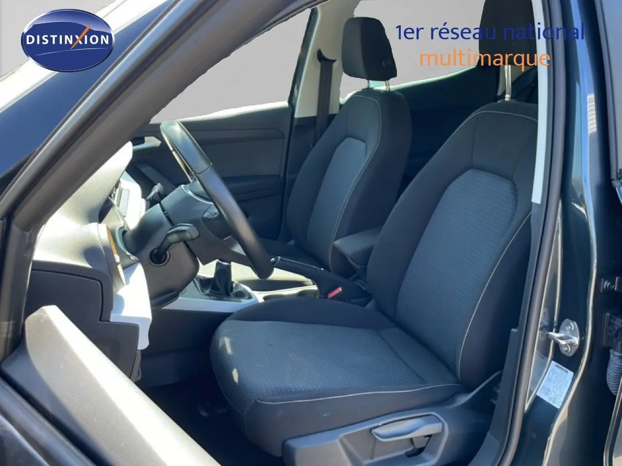 Vue intérieure côté conducteur du SEAT Arona 2025, sièges tissu gris foncé et volant cuir multifonction.