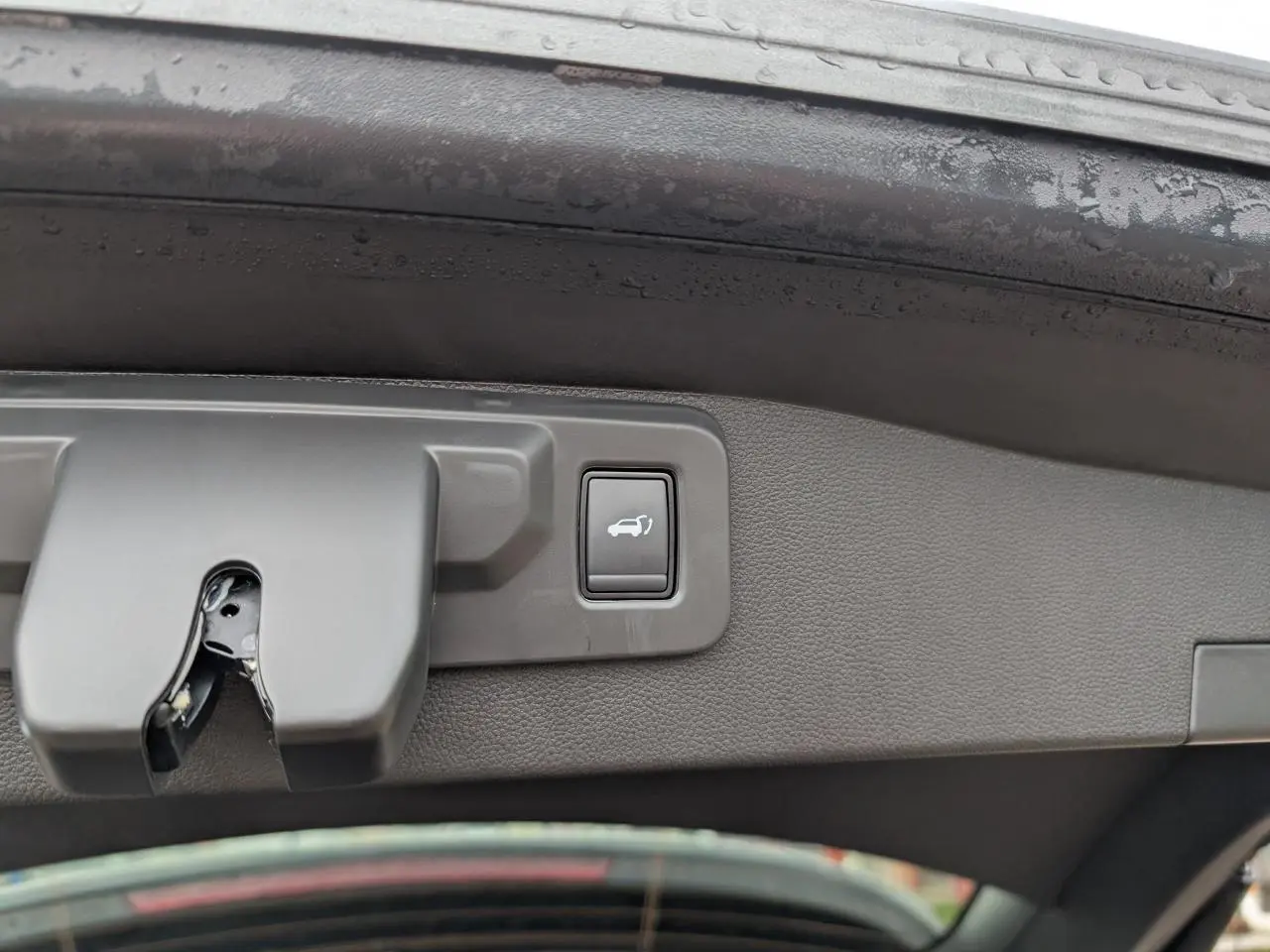 Gros plan sur le bouton d'ouverture électrique du hayon du Renault Austral gris, vu depuis l'intérieur du coffre.