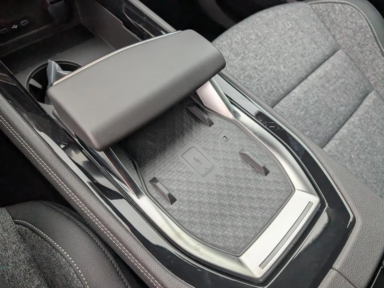 Gros plan sur la console centrale noire avec chargeur smartphone à induction et accoudoir gris du Renault Austral 2025.