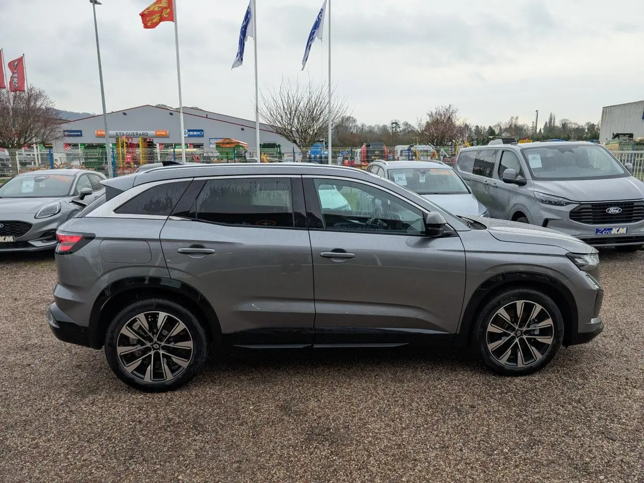 Vue de profil droit du Renault Austral gris avec jantes alliage noires diamantées sur un parking extérieur.