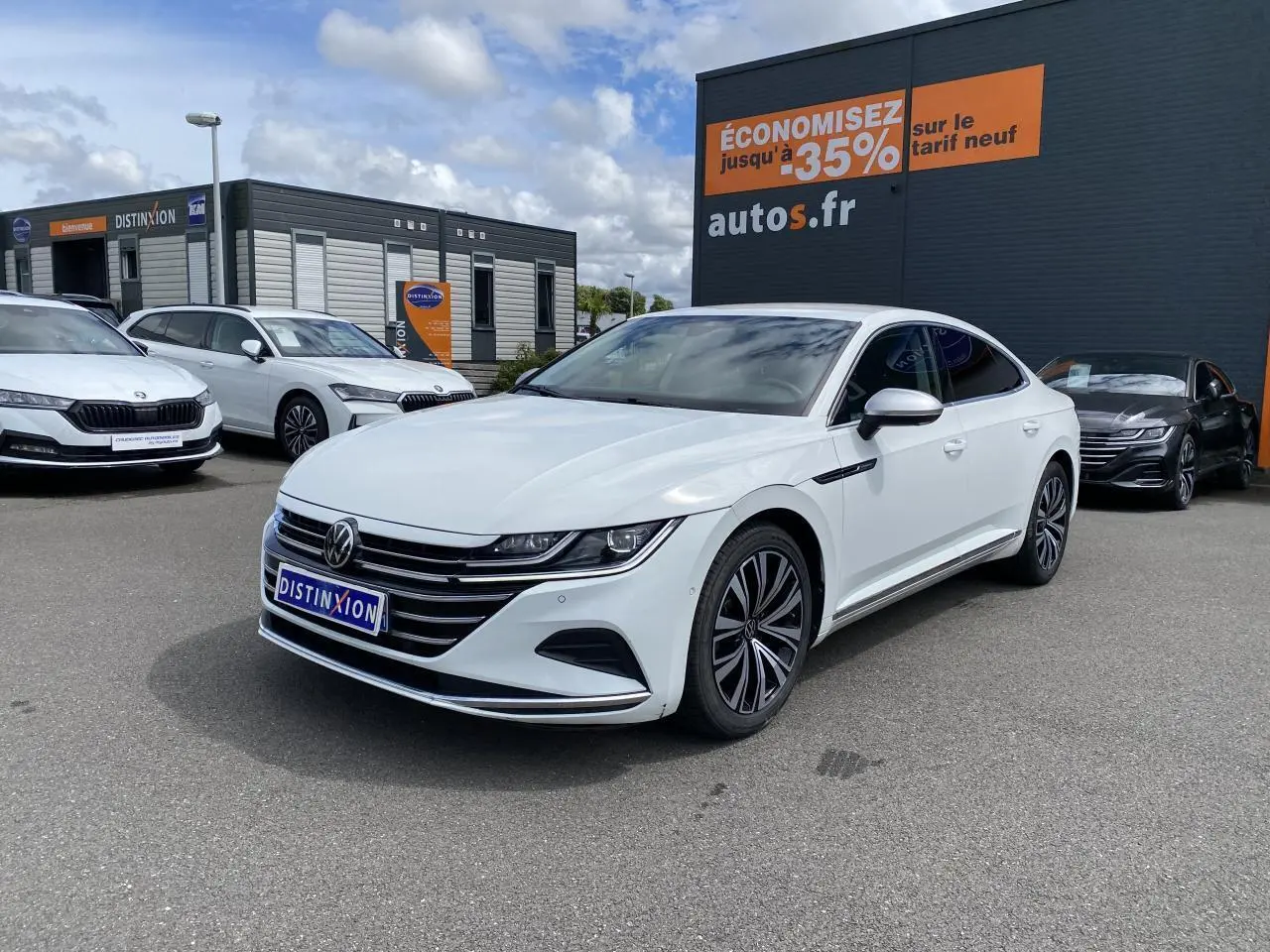 Volkswagen Arteon blanc pur vu en 3/4 avant droit sur parking devant un bâtiment commercial.