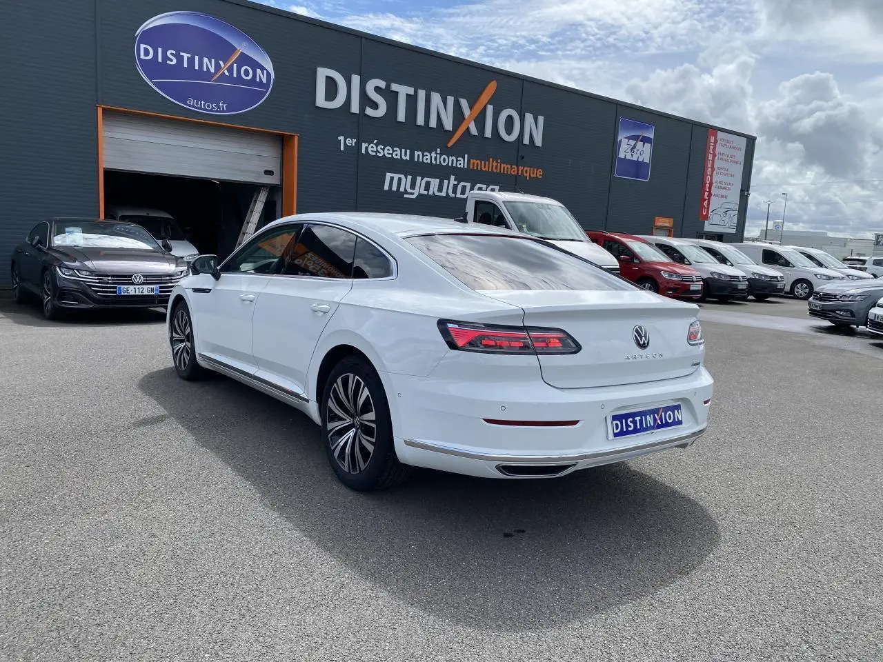 Vue 3/4 arrière droite d'une Volkswagen Arteon blanc pur avec feux arrière LED et jantes alliage sur parking extérieur.
