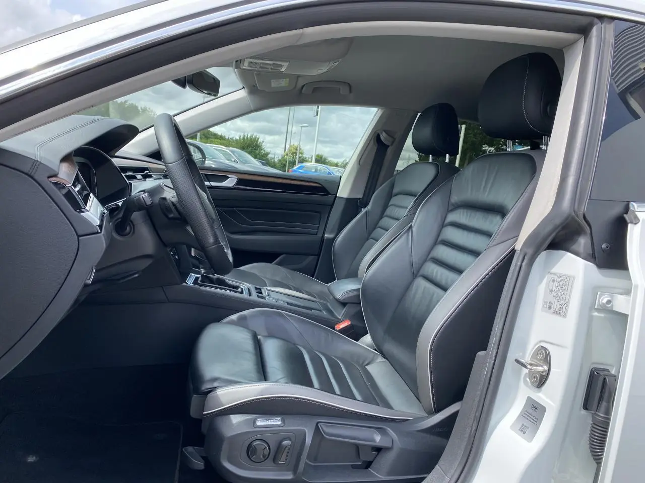 Vue intérieure côté conducteur du Volkswagen Arteon blanc pur 2022, sièges avant en cuir Nappa noir avec finitions bois précieux.