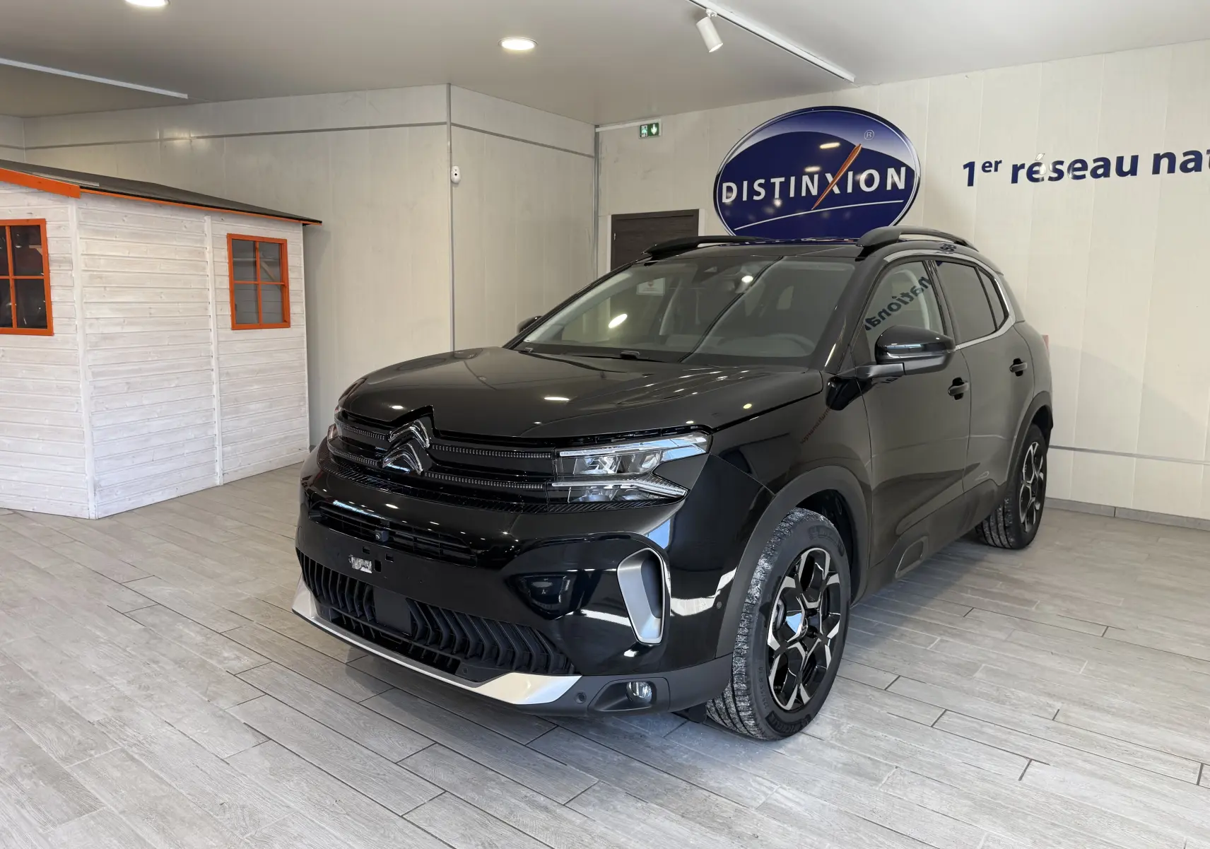 Vue 3/4 avant droit d'un Citroën C5 Aircross noir brillant avec jantes noires et détails chromés en showroom.
