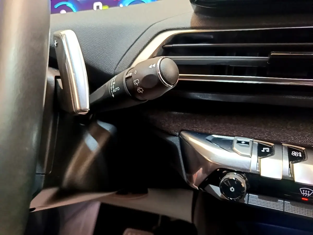 Détail du commodo d’essuie-glace et partie de la console centrale noire du Peugeot 3008 hybride gris foncé, vue intérieure.