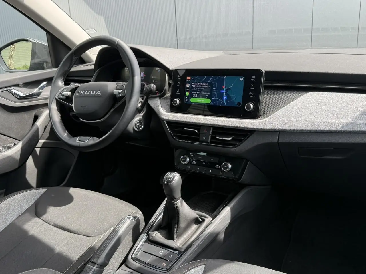 Vue intérieure côté conducteur du Skoda Scala TSI 116 gris graphite, volant cuir, écran tactile et levier de vitesses manuel.
