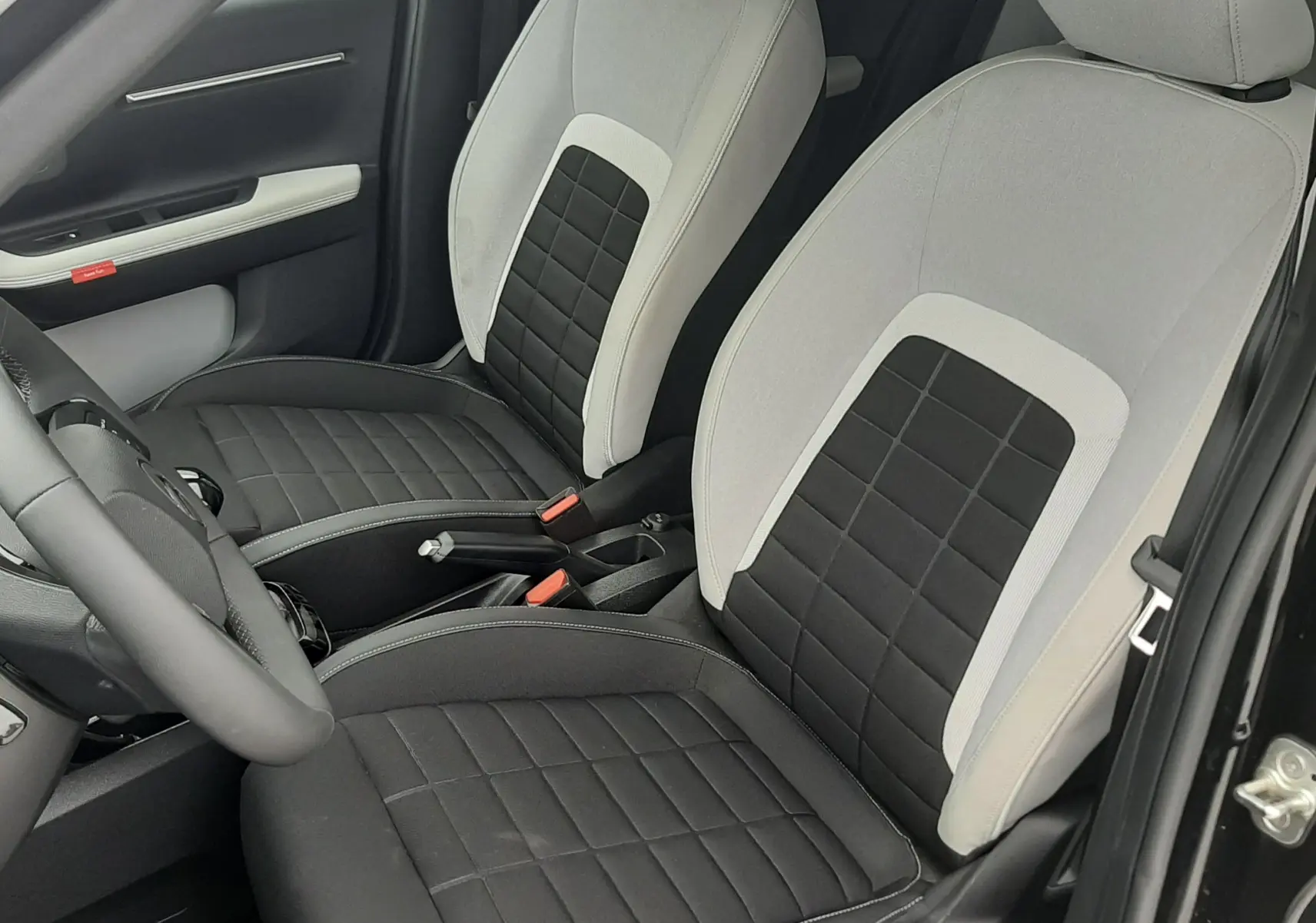 Vue intérieure en gros plan des sièges avant bi-matière noir et blanc de la Citroën C3 2025, porte ouverte côté conducteur.