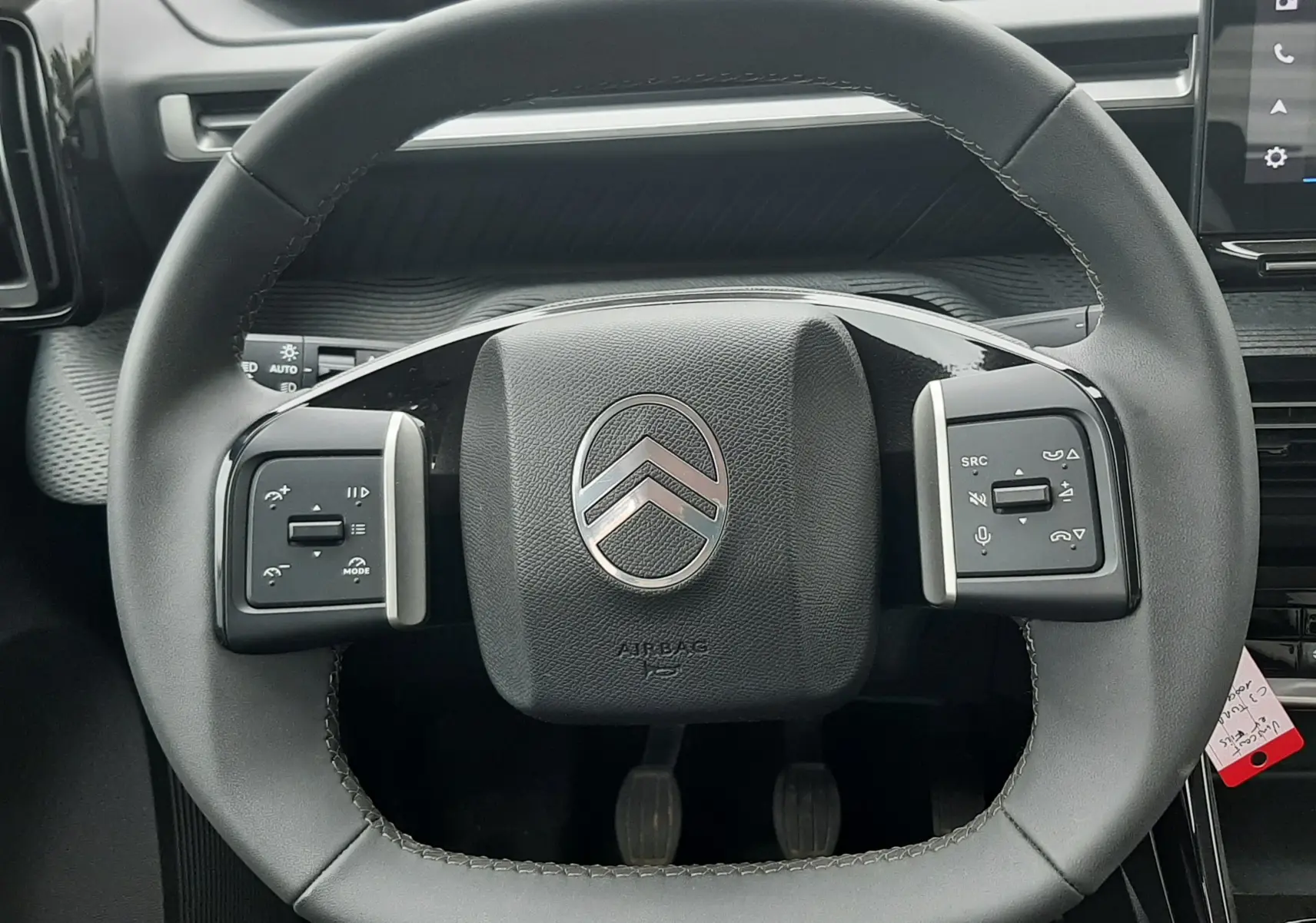 Vue rapprochée du volant noir de la Citroën C3 2025, avec commandes intégrées et logo argenté central.
