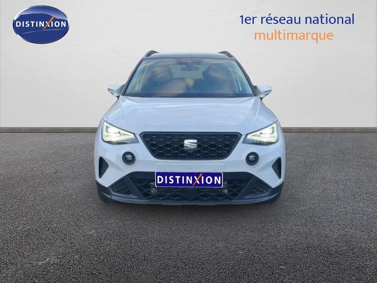 Vue frontale d'un SEAT Arona blanc avec toit gris, phares LED allumés et calandre noire distinctive.