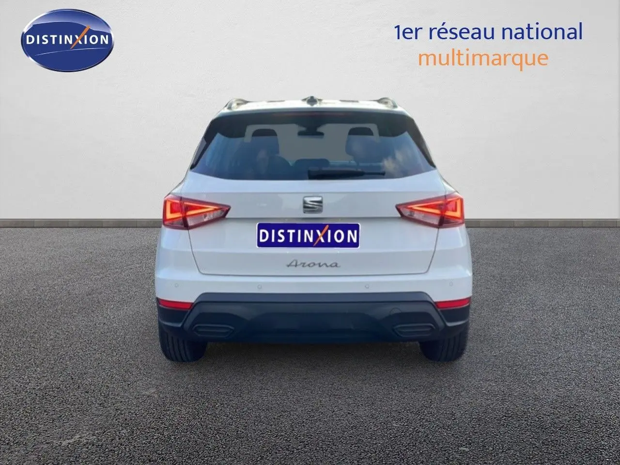 Vue arrière d'un SEAT Arona blanc avec toit gris, feux allumés et logo Distinxion visible sur fond neutre.