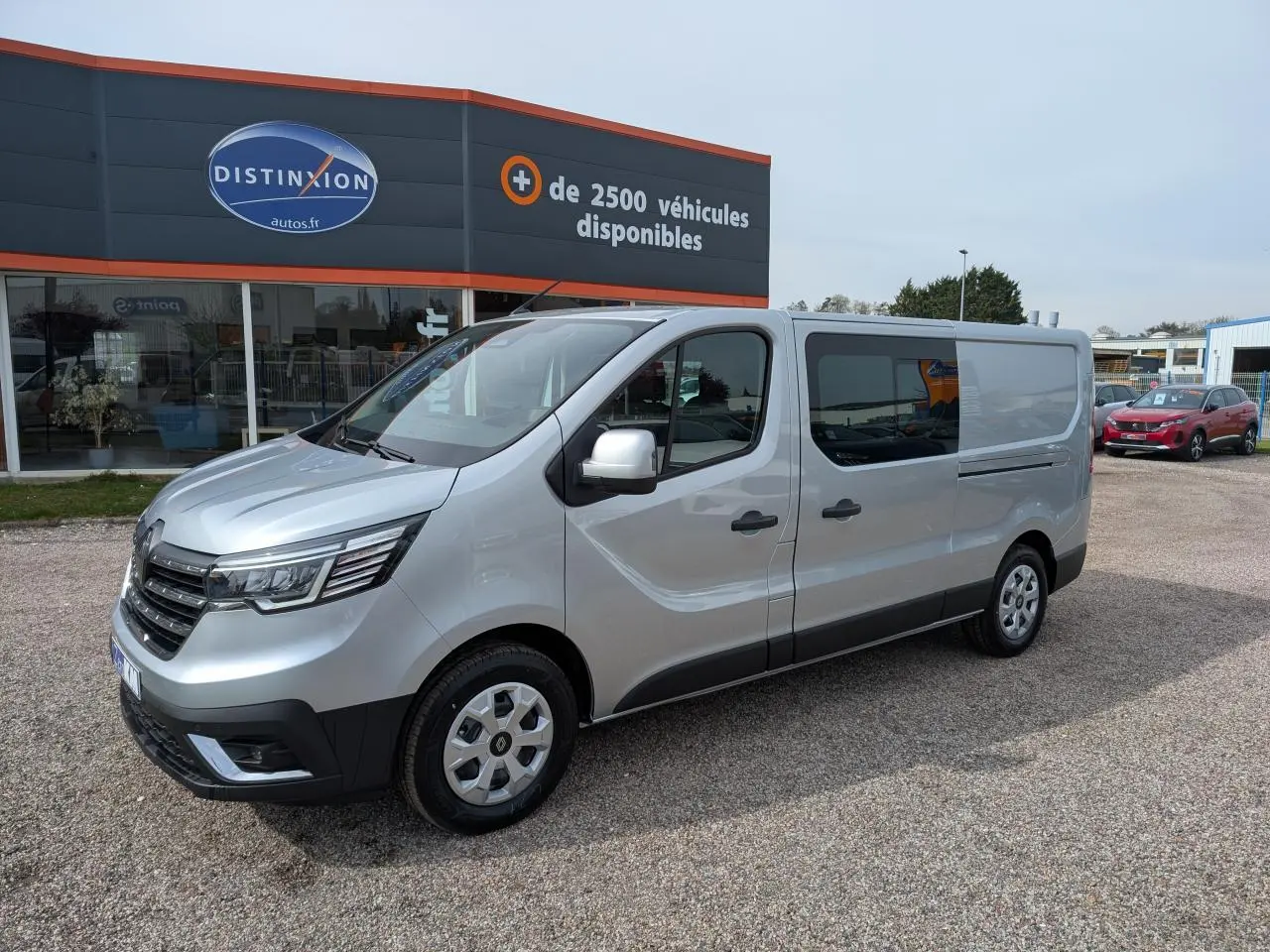 Renault Trafic Fourgon gris Highland en 3/4 avant droit, avec portes latérales vitrées et enjoliveurs 16 pouces.