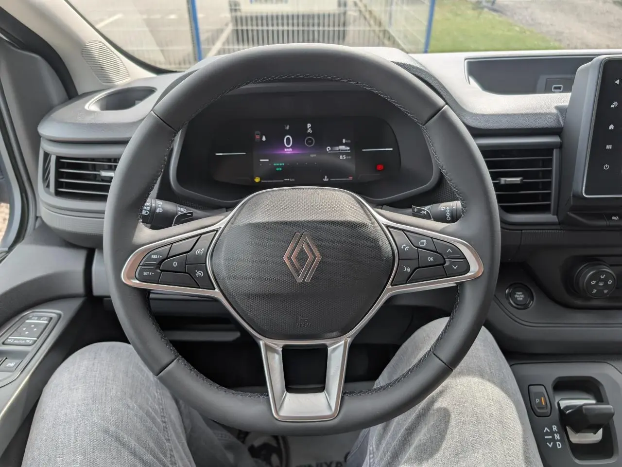 Vue rapprochée du volant noir et du combiné numérique du Renault Trafic Fourgon gris, avec commandes intégrées et tableau de bord moderne.