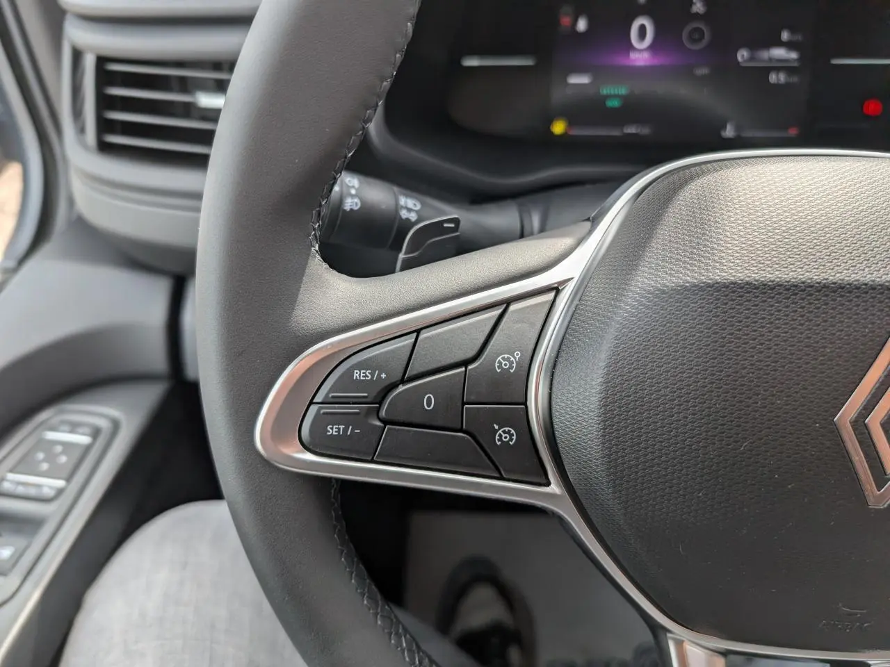 Gros plan sur le volant noir du Renault Trafic Fourgon 2025 avec commandes de régulateur de vitesse et tableau de bord numérique.