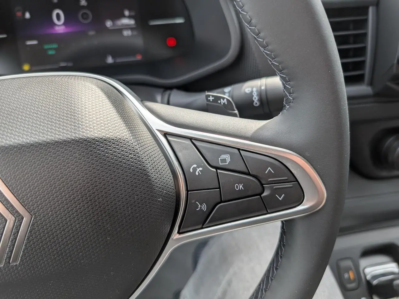 Gros plan sur les commandes à droite du volant noir du Renault Trafic Fourgon gris, avec affichage numérique en arrière-plan.