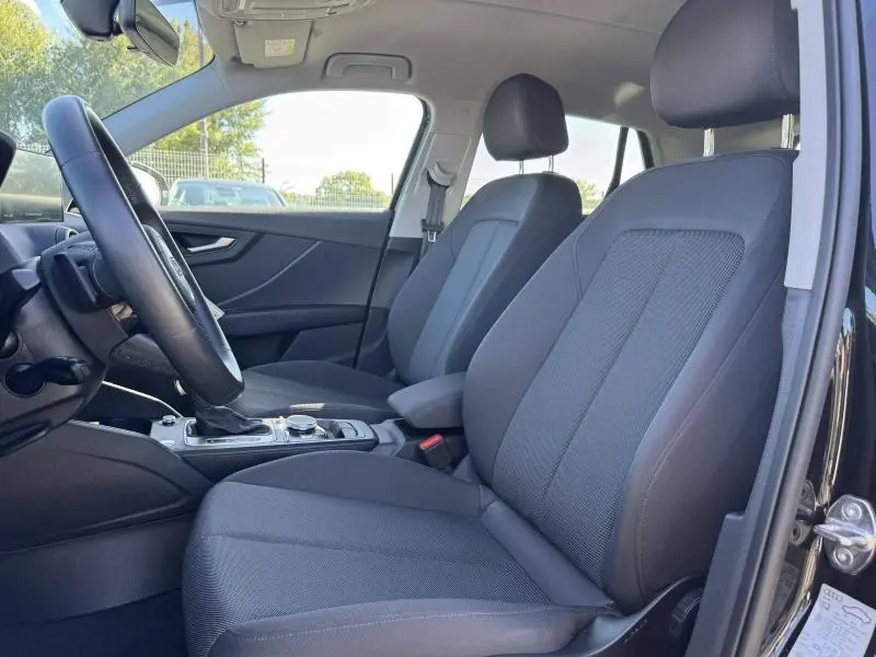 Vue intérieure côté conducteur de l'Audi Q2 35 TFSI 2023 avec sièges tissu noirs et console centrale moderne.