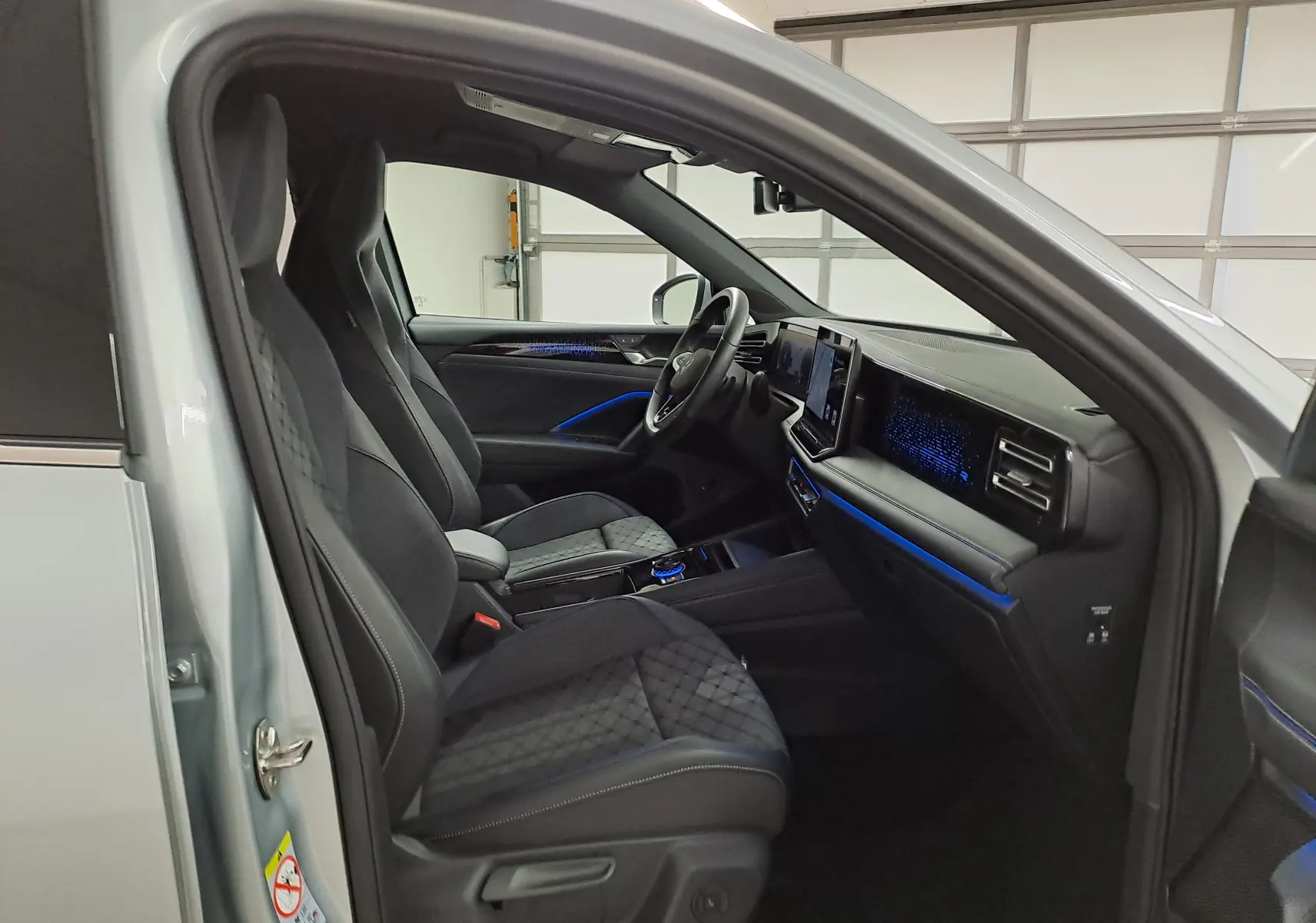 Vue intérieure côté conducteur du Volkswagen Tiguan 2025 argent Dolomite, avec sièges noirs et éclairage d'ambiance bleu.