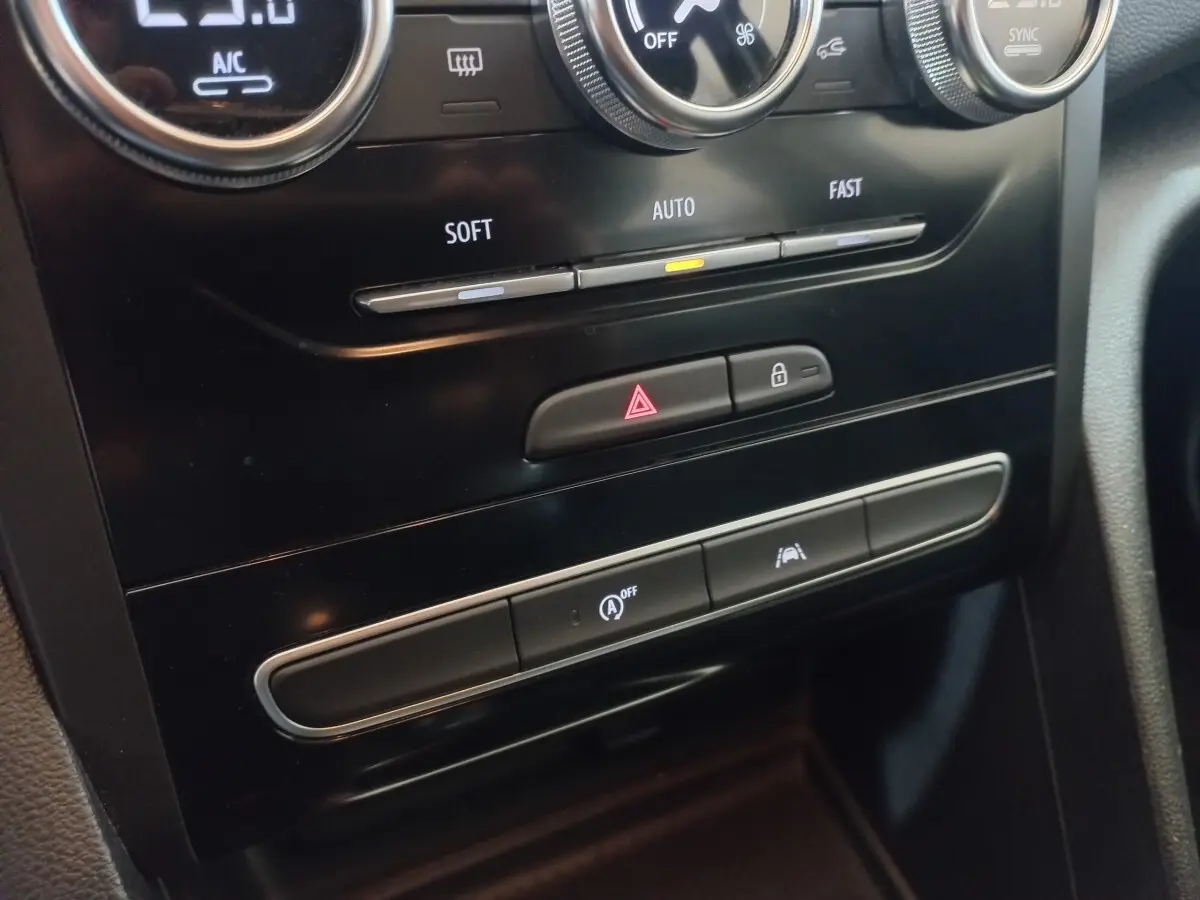 Gros plan sur la console centrale noire de la Renault Mégane Business TCe 115, montrant les commandes climatisation et boutons de sécurité.