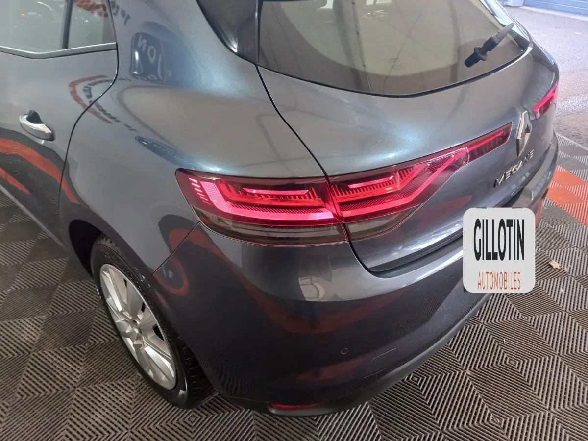 Vue 3/4 arrière droite d'une Renault Mégane Business gris foncé avec feux arrière LED allumés dans un garage.