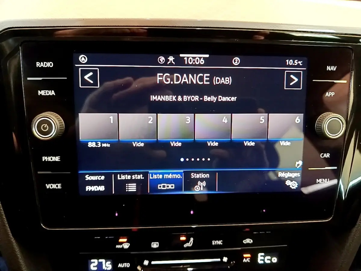 Écran tactile central affichant la radio digitale dans un Volkswagen Passat blanc, vue intérieure frontale.