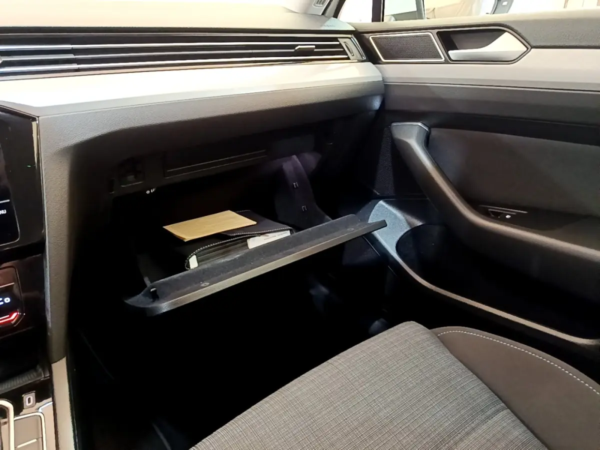 Intérieur de Volkswagen Passat hybride 2021, vue côté passager sur boîte à gants ouverte et siège tissu gris.