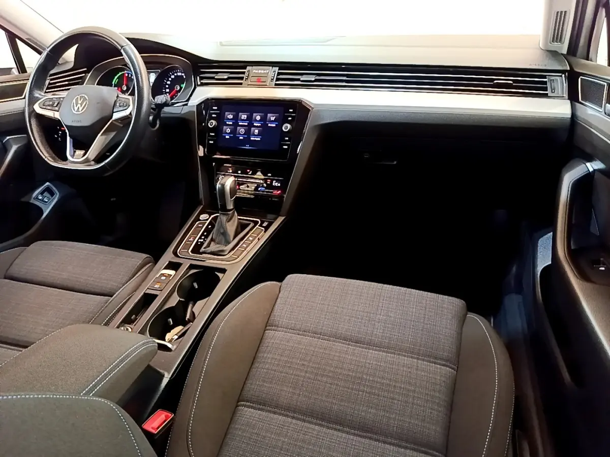 Vue intérieure avant droite de la Volkswagen Passat hybride avec tableau de bord noir, écran tactile et sièges tissu gris.