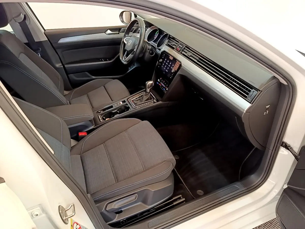 Intérieur avant droit de la Volkswagen Passat blanche, montrant sièges tissu gris et tableau de bord avec écran tactile.
