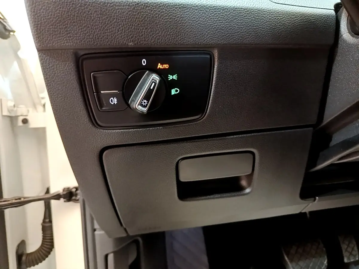 Détail du tableau de bord côté gauche avec commande des phares et partie de la portière blanche d'une Volkswagen Passat hybride.