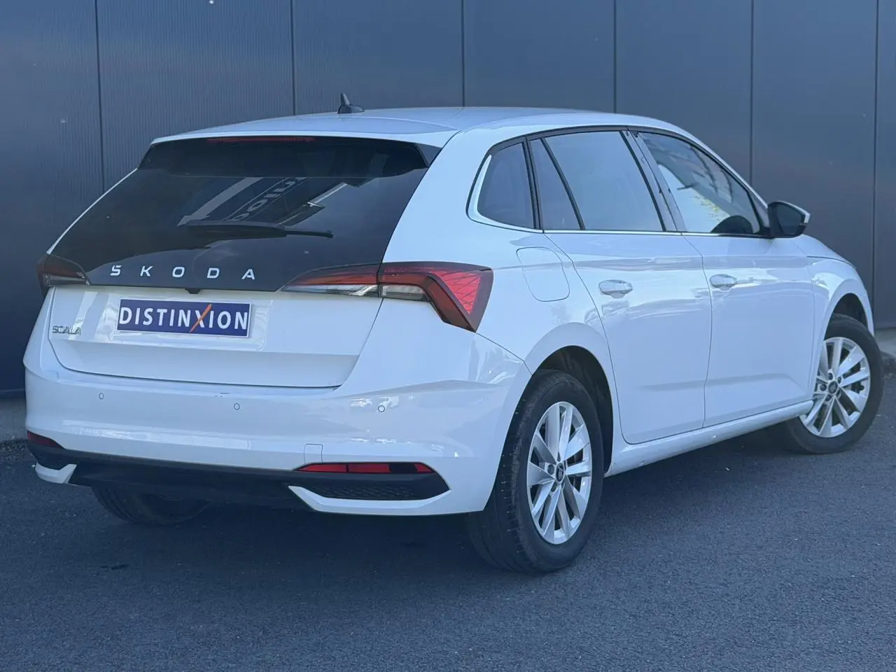 Vue 3/4 arrière droite d'une Skoda Scala blanc glacier avec lunette arrière surteintée et jantes alliage 16 pouces.