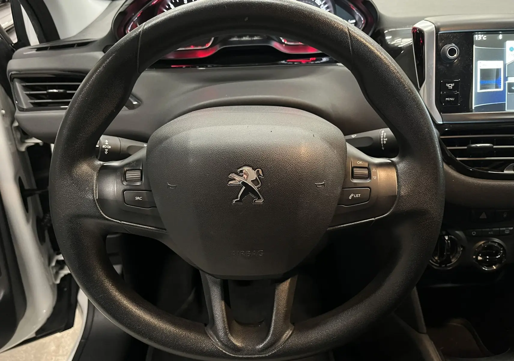 Vue rapprochée du volant noir de la Peugeot 208 blanche de 2014, avec tableau de bord et écran tactile visibles.
