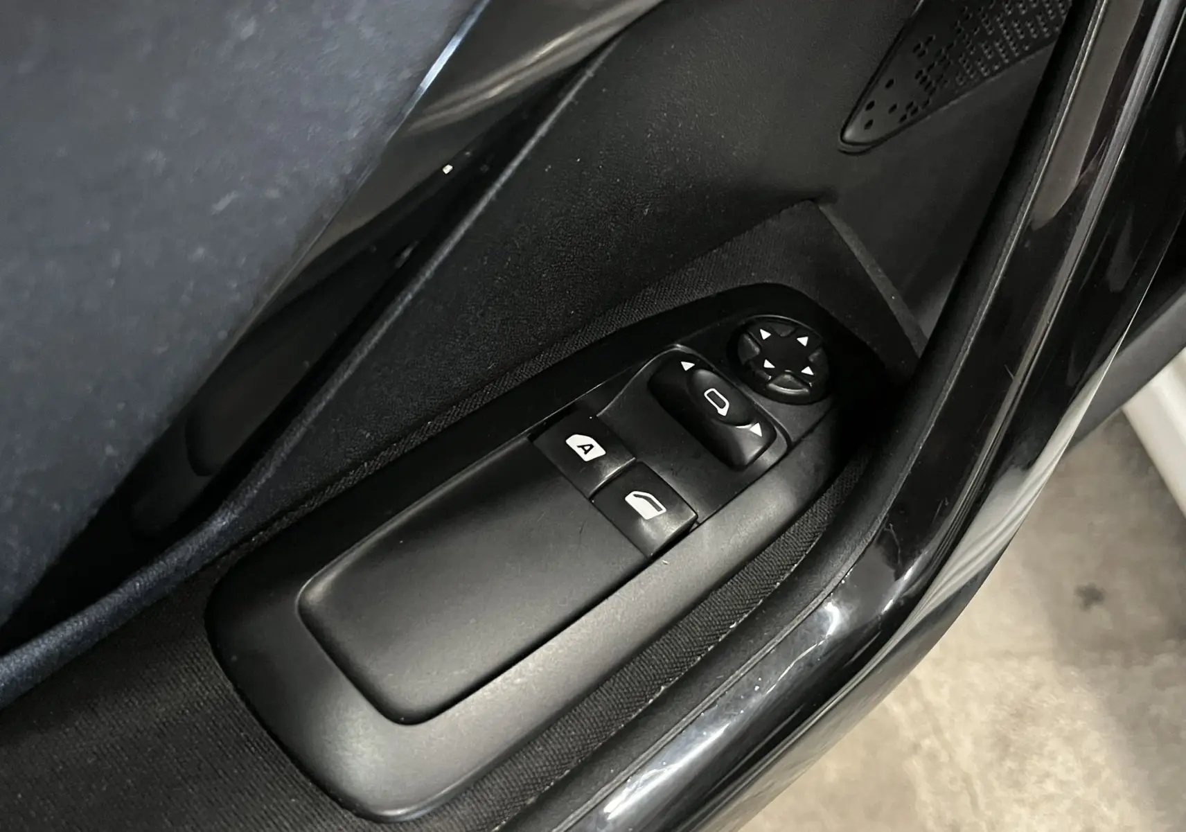 Gros plan sur les commandes de lève-vitres et réglage des rétroviseurs côté conducteur d'une Peugeot 208 blanche de 2014.