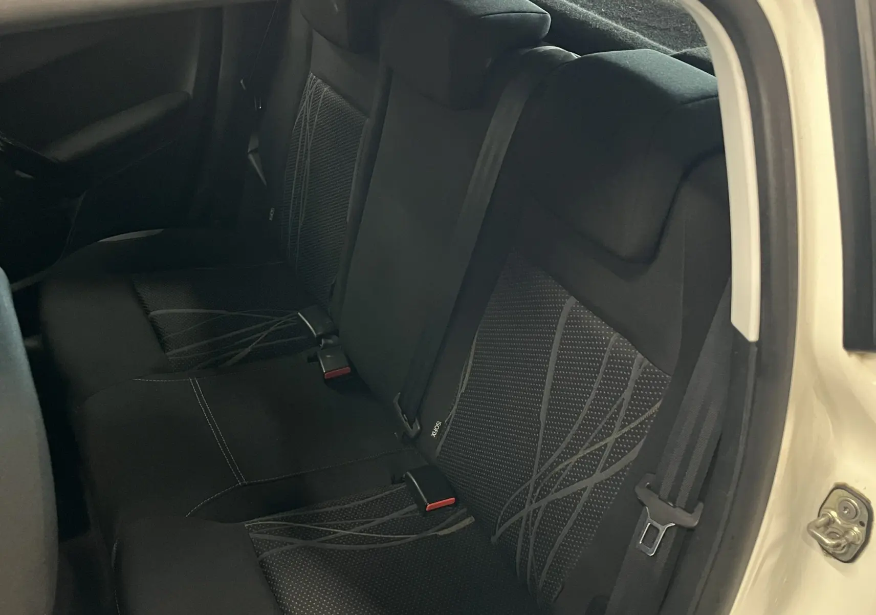 Vue intérieure arrière côté droit montrant les sièges noirs en tissu avec motifs gris d'une Peugeot 208 blanche de 2014.