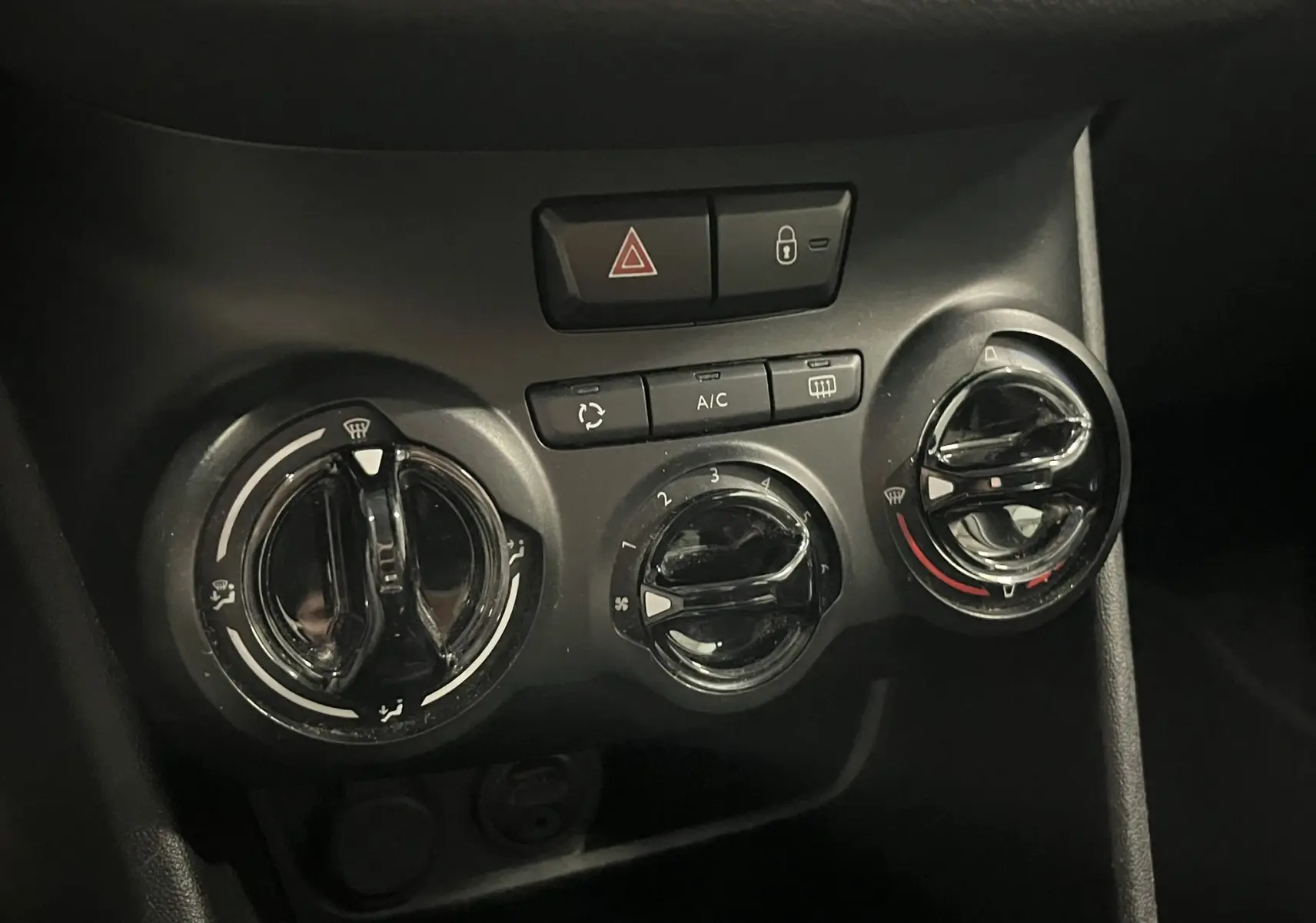 Gros plan sur les commandes de climatisation noires de la Peugeot 208 blanche, avec boutons de réglage et ventilation.