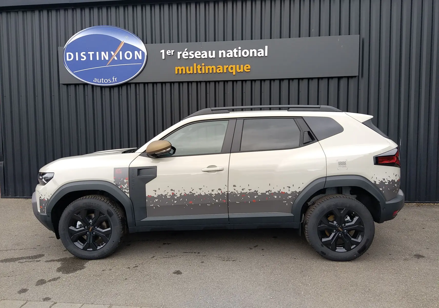 Vue de profil droit du Dacia Duster Hybrid-G 150 ch en couleur Sandstone avec motifs pixelisés gris et noir sur bas de caisse.