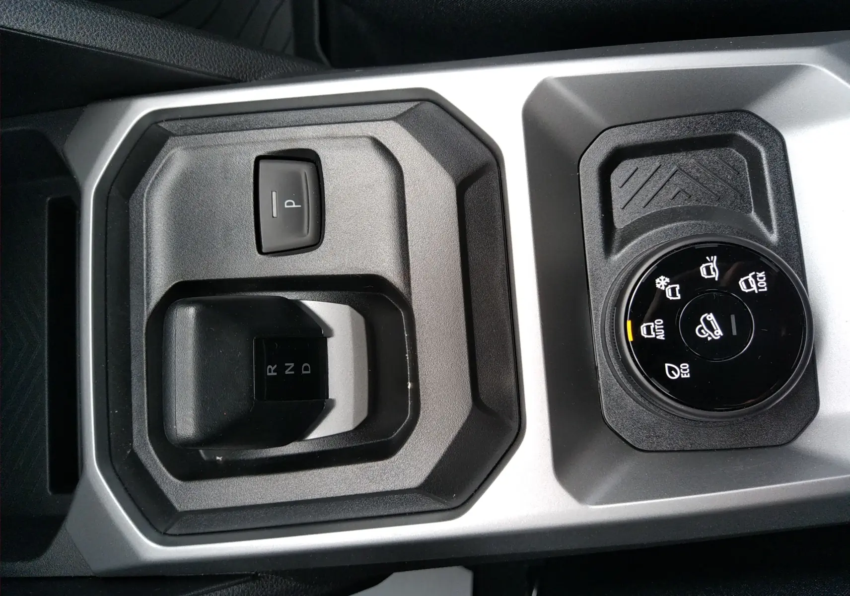 Vue rapprochée de la console centrale grise du Dacia Duster Hybrid-G 150 ch, avec sélecteur de boîte auto et molette de modes de conduite.